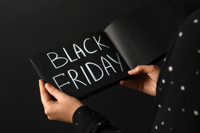 Photo of Woman holding notebook with words Black Friday on dark background, closeup