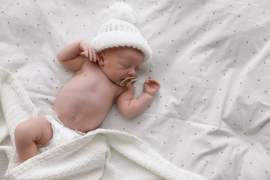 Photo of Cute newborn baby in white knitted hat sleeping on bed, top view. Space for text