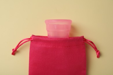 Cotton bag with menstrual cup on beige background, top view
