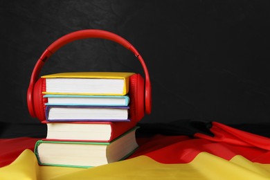 Learning foreign language. Different books and headphones on flag of Germany, space for text