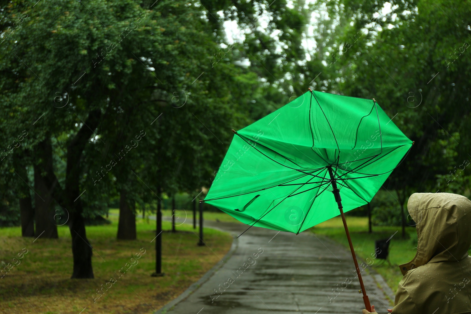 Photo of Woman with broken green umbrella in park on rainy day