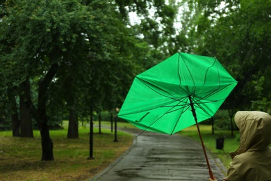 Photo of Woman with broken green umbrella in park on rainy day