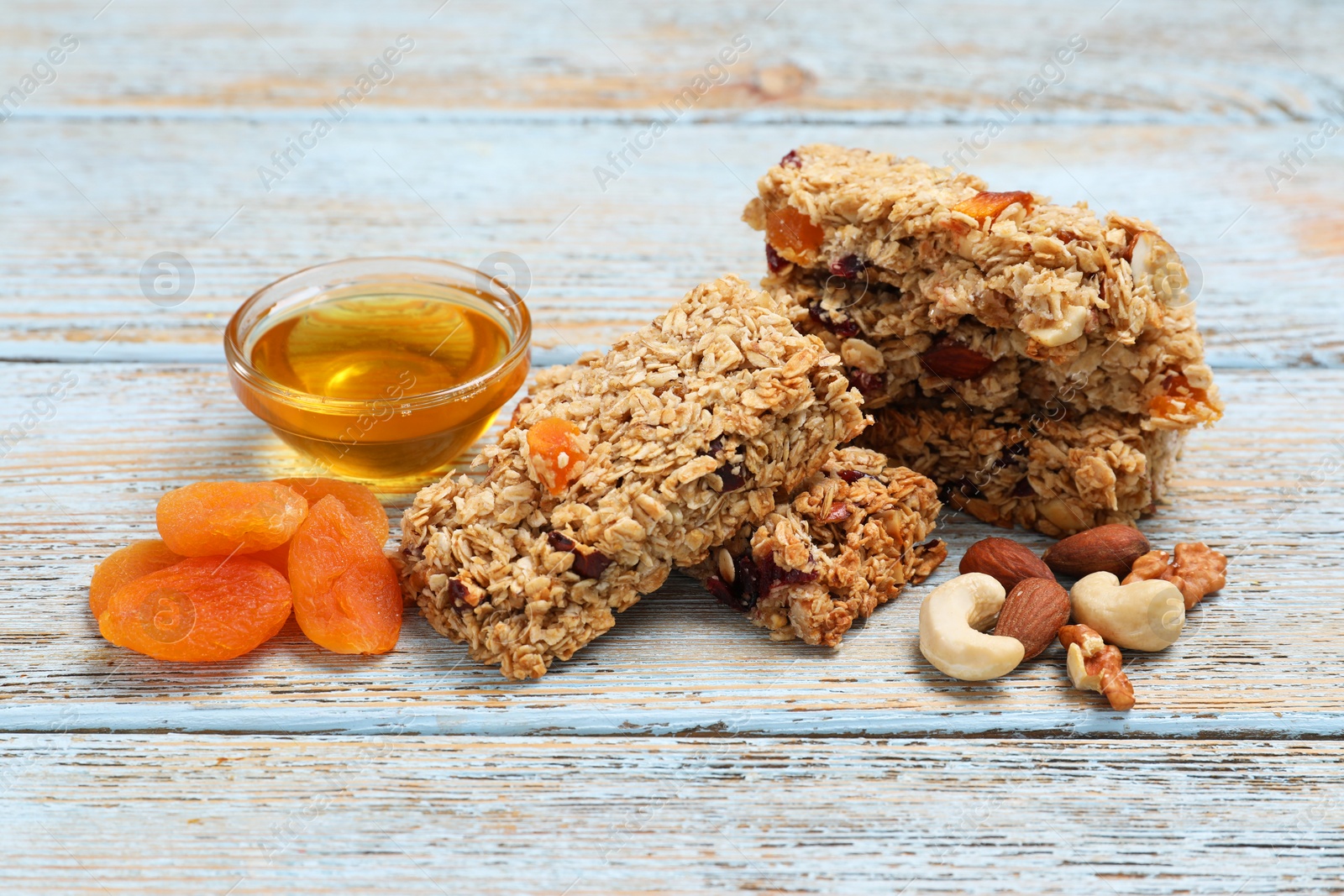 Photo of Tasty granola bars and ingredients on light blue wooden table