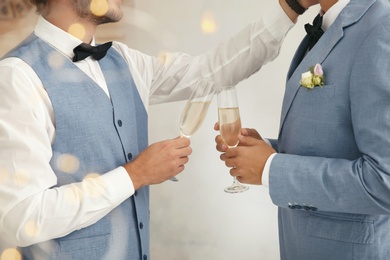 Photo of Newlywed gay couple with glasses of champagne at home, closeup