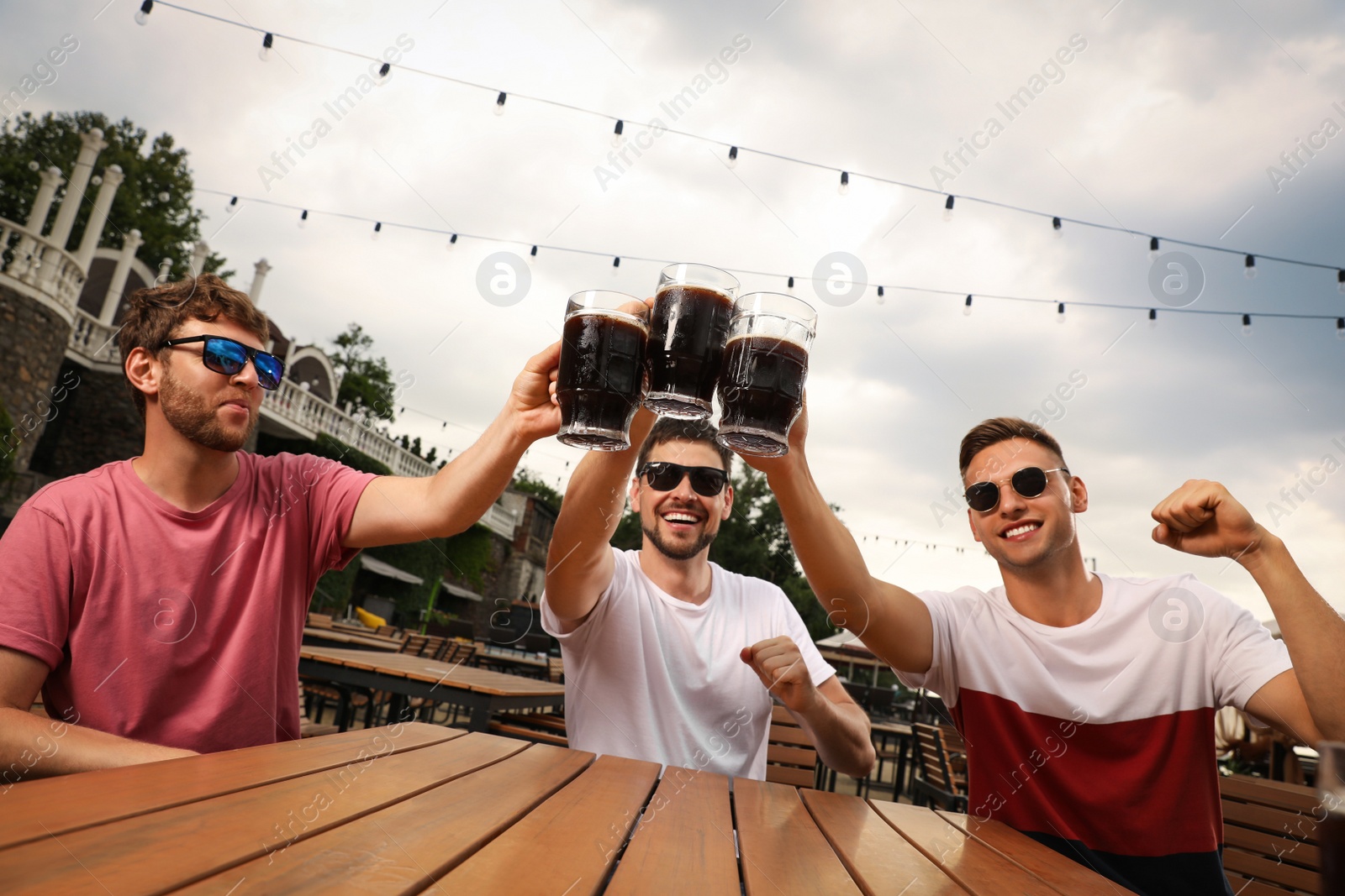 Photo of Friends clinking glasses of beer in outdoor cafe