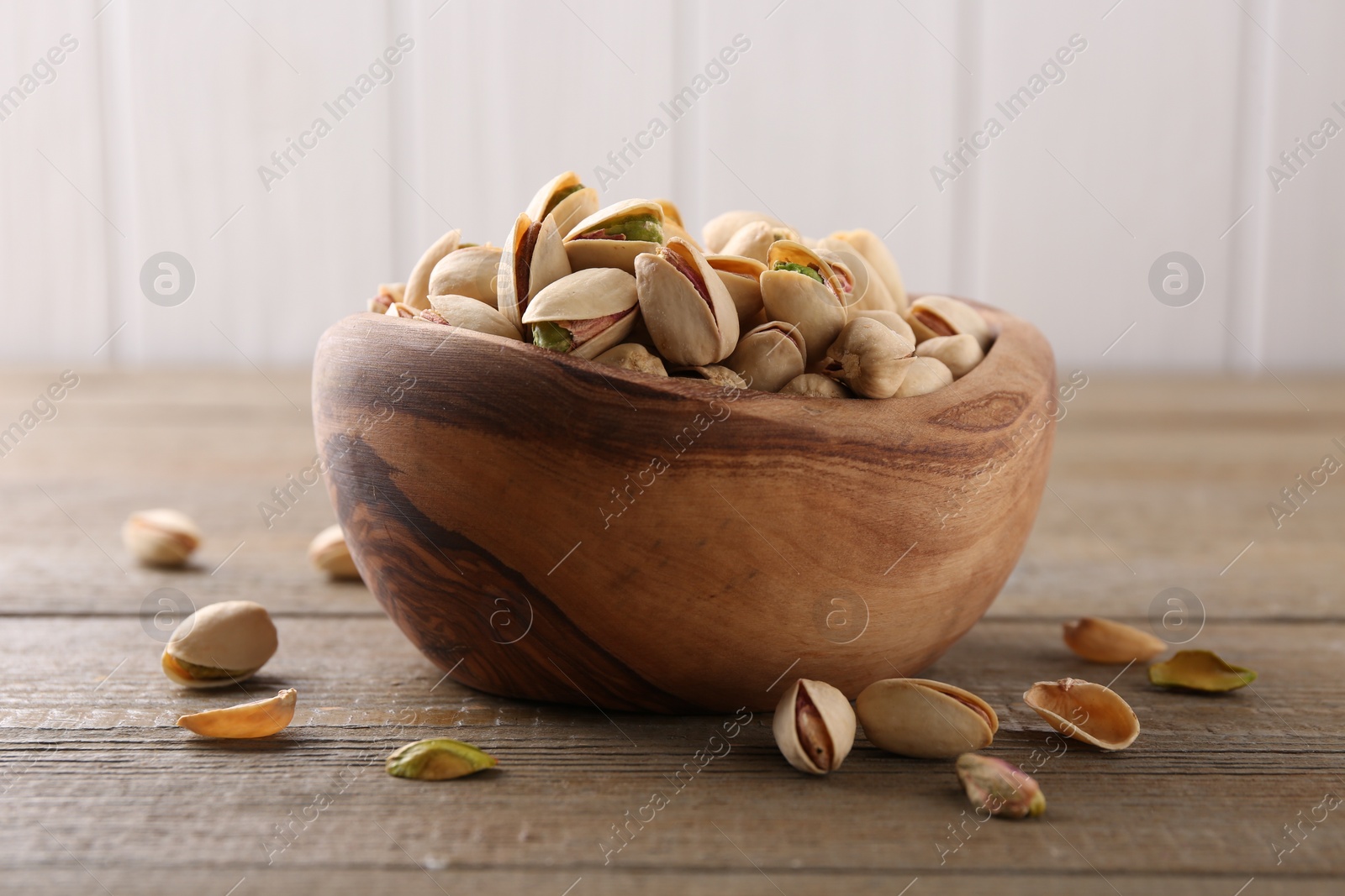 Photo of Tasty pistachios in bowl on wooden table, closeup