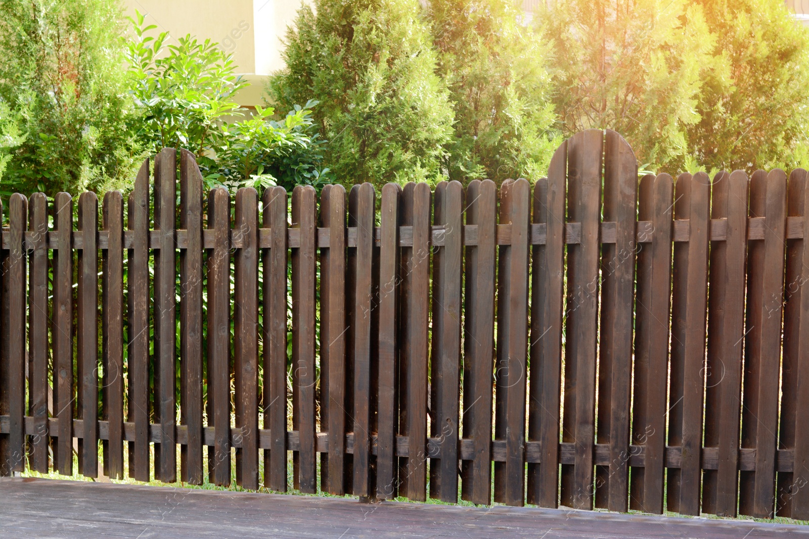 Photo of Wooden fence near beautiful trees on sunny day outdoors
