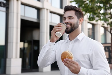 Photo of Businessman with hamburger and paper cup of coffee having lunch outdoors
