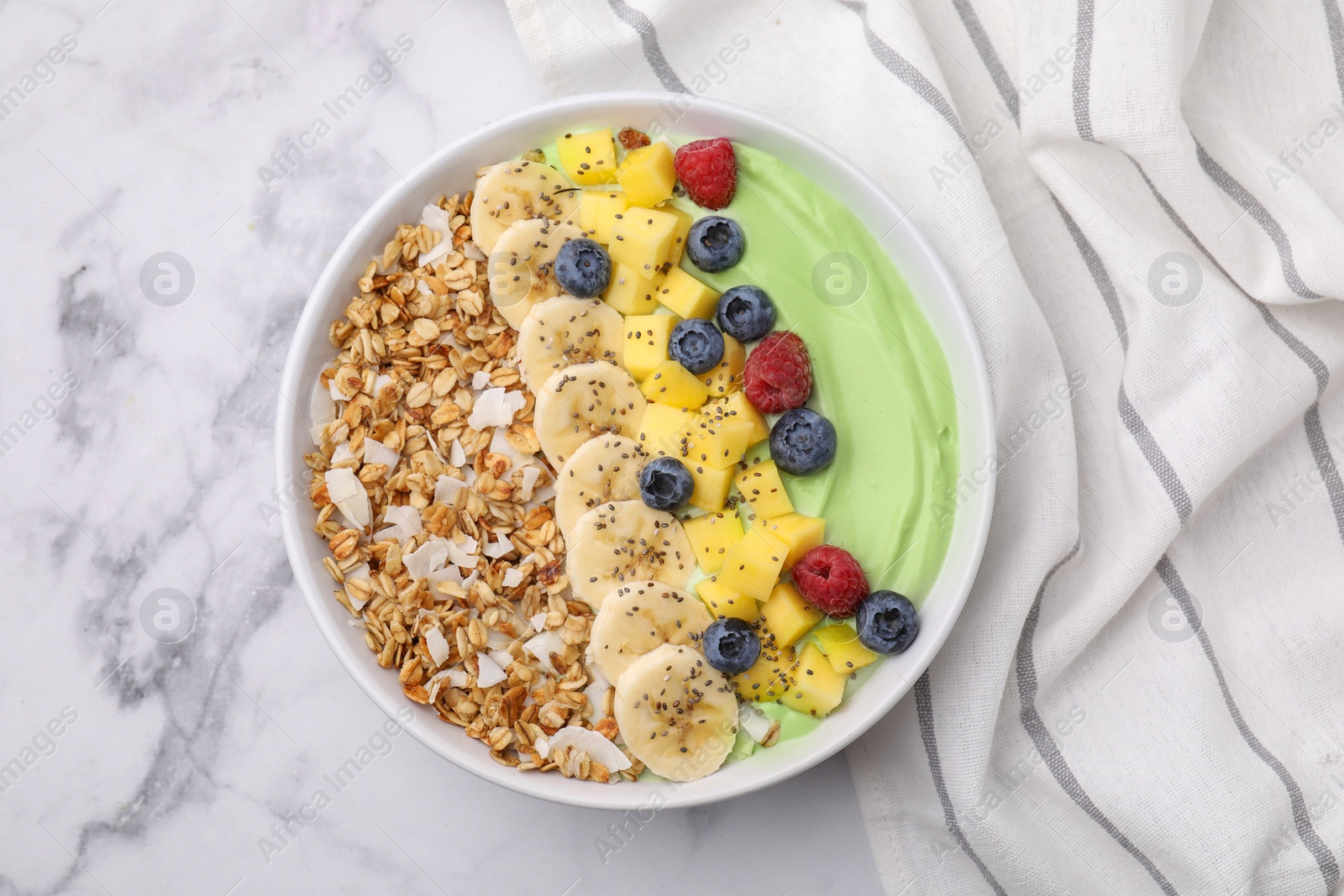 Photo of Tasty matcha smoothie bowl served with fresh fruits and oatmeal on white marble table, top view. Healthy breakfast