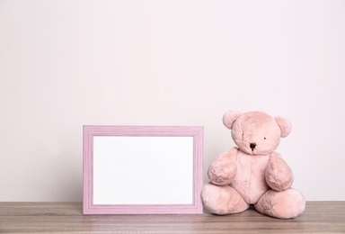 Photo of Photo frame and adorable teddy bear on table against light background, space for text. Child room elements
