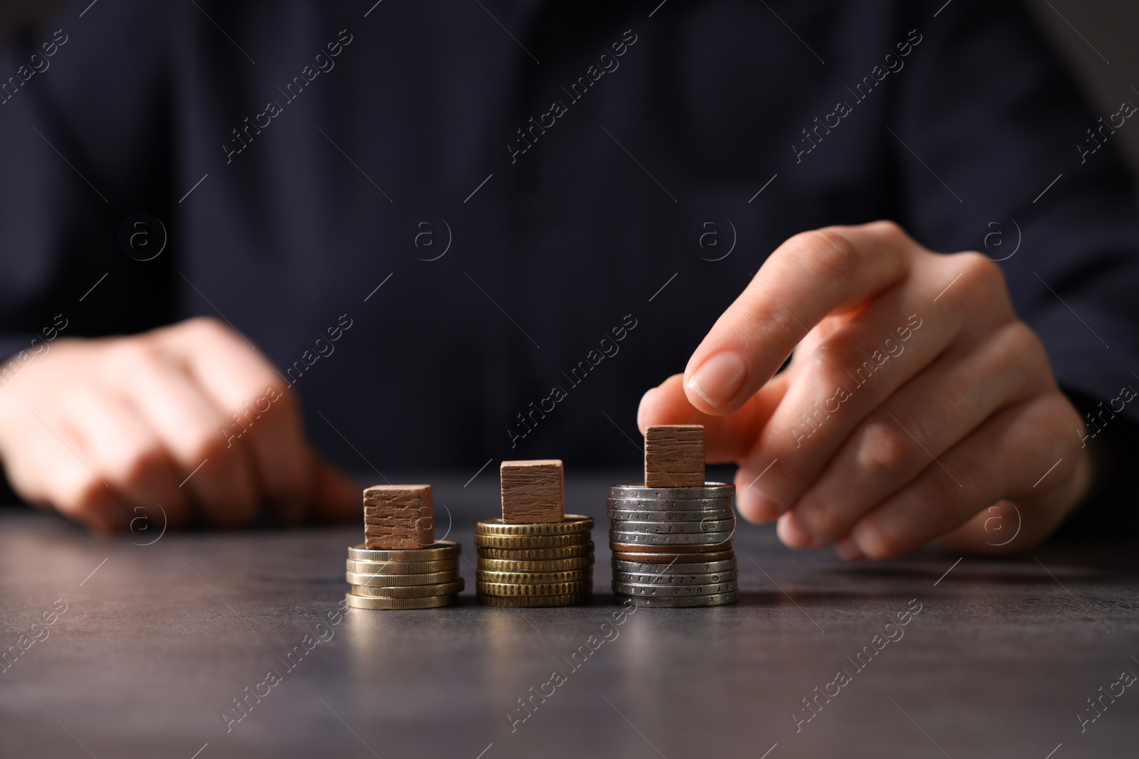 Photo of Taxes. Woman with wooden cubes and coins at grey table, closeup