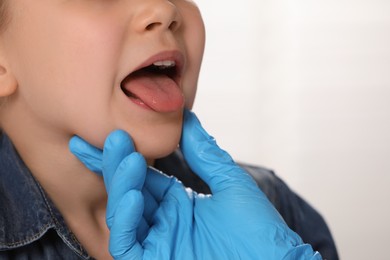 Photo of Doctor in medical glove examining girl`s oral cavity on light grey background, closeup. Space for text