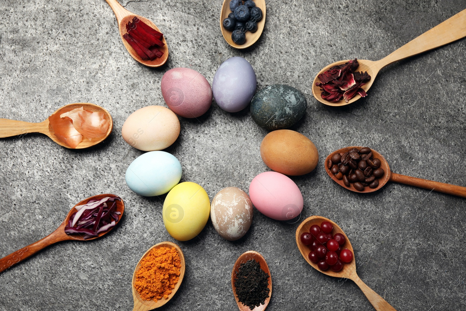 Photo of Naturally painted Easter eggs on grey table, flat lay. Turmeric, cranberries, red cabbage, onion, beetroot, blueberries, hibiscus, coffee beans and tea used for coloring