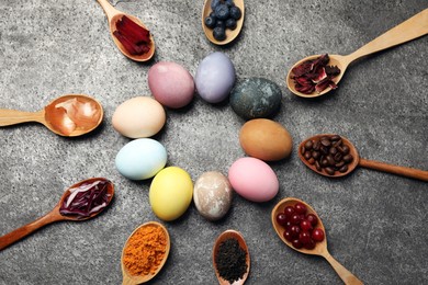 Naturally painted Easter eggs on grey table, flat lay. Turmeric, cranberries, red cabbage, onion, beetroot, blueberries, hibiscus, coffee beans and tea used for coloring