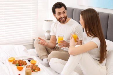 Photo of Happy couple having breakfast and talking on bed at home