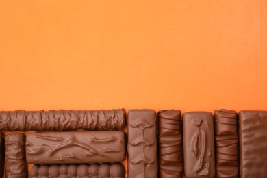 Photo of Different tasty chocolate bars on orange background, flat lay. Space for text