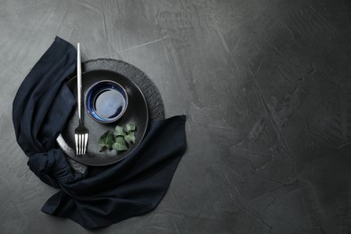 Stylish table setting. Dishes, fork, napkin and green leaves on grey surface, top view with space for text