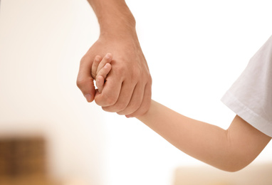 Photo of Father holding hands with his child indoors, closeup. Happy family