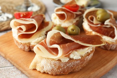 Photo of Tasty sandwiches with cured ham, tomatoes and olives on wooden board, closeup