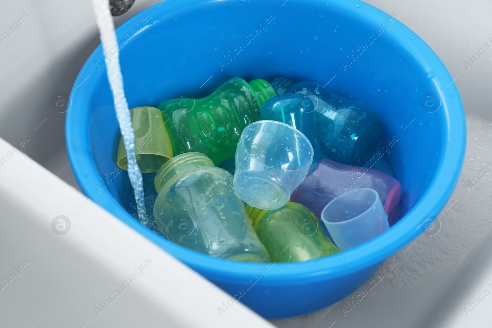 Photo of Light blue basin with baby bottles under stream of water in sink