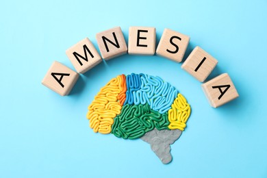 Word Amnesia and brain with sections made of plasticine on light blue background, flat lay