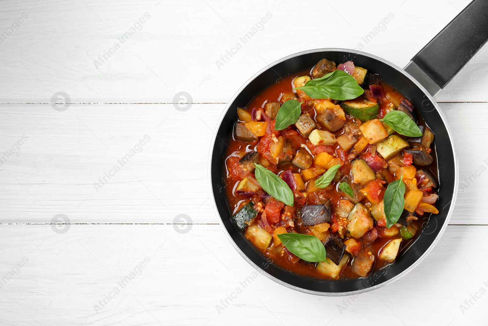 Photo of Frying pan with tasty ratatouille on white wooden table, top view. Space for text