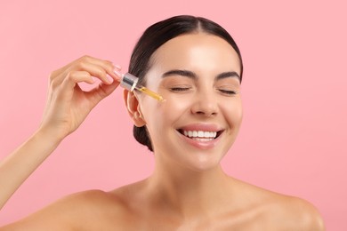 Photo of Beautiful young woman applying serum onto her face on pink background