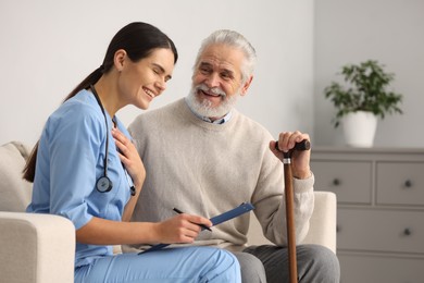 Photo of Health care and support. Nurse holding clipboard and laughing with elderly patient in hospital