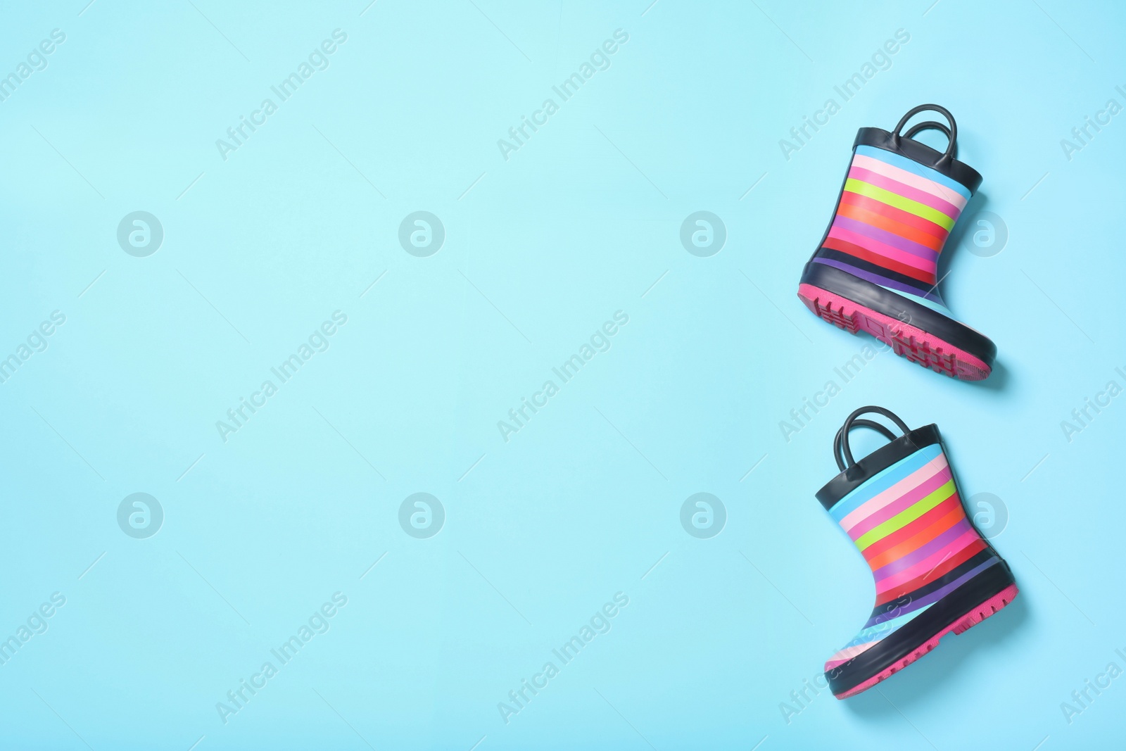 Photo of Striped rubber boots on light blue background, top view. Space for text