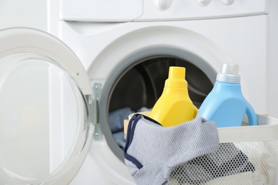 Photo of Bottles of detergent and children's clothes in basket near washing machine