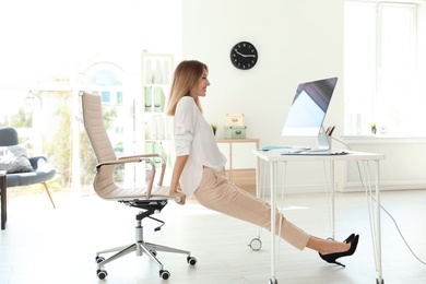 Photo of Young beautiful businesswoman stretching in office. Workplace fitness