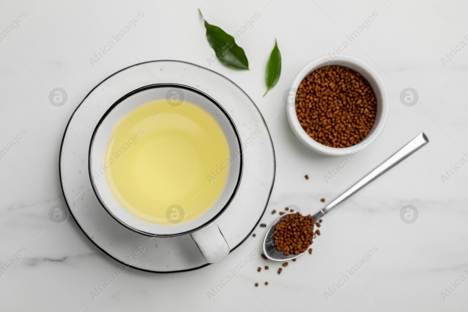 Photo of Cup of buckwheat tea and granules on white marble table, flat lay