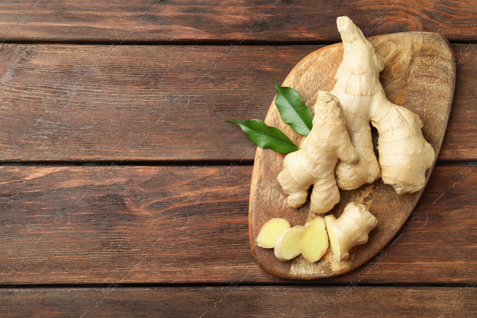 Photo of Cut and whole fresh ginger with leaves on wooden table, top view. Space for text