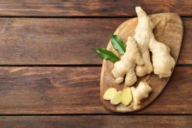 Photo of Cut and whole fresh ginger with leaves on wooden table, top view. Space for text