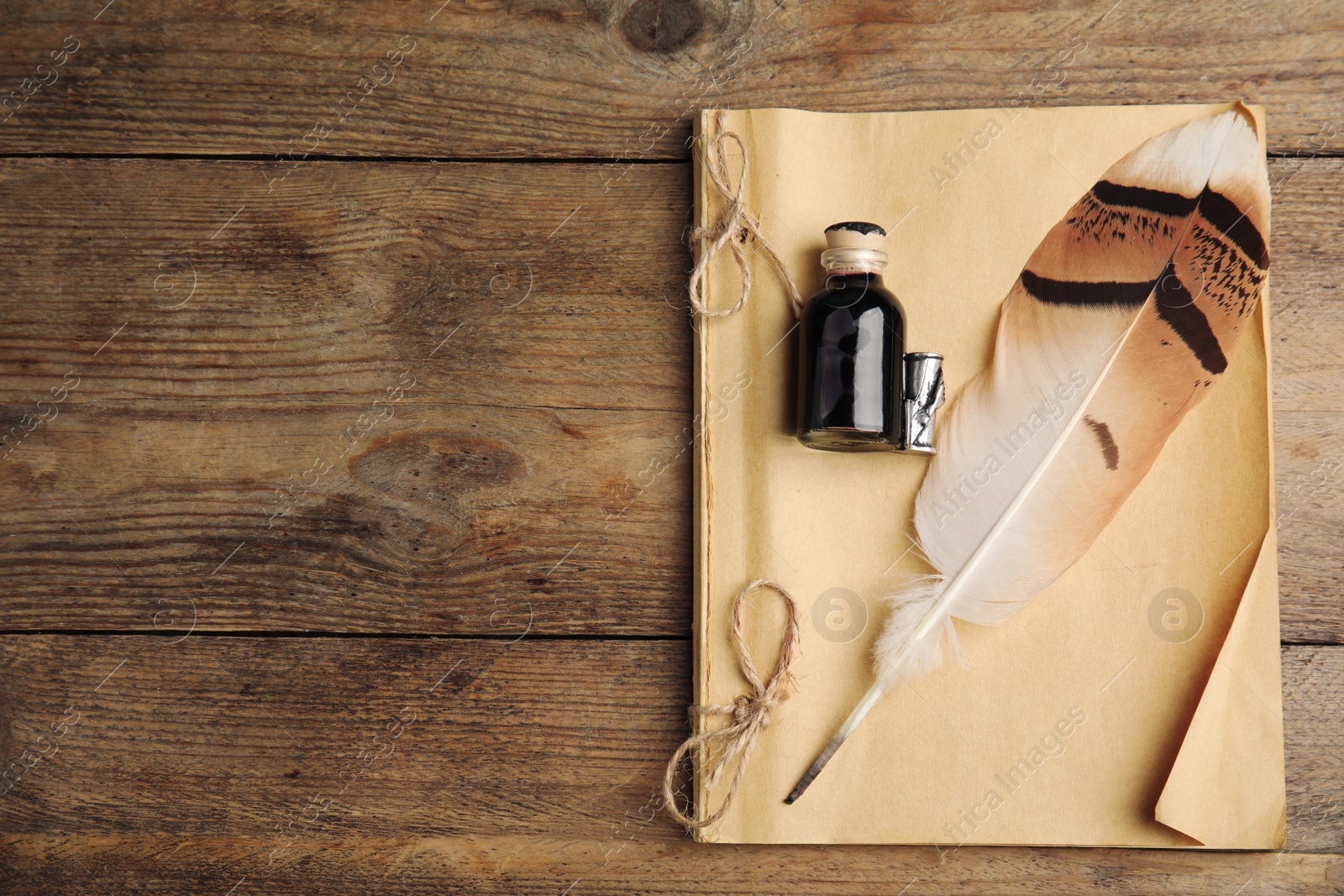 Photo of Feather pen, bottle of ink and notebook on wooden table, top view. Space for text