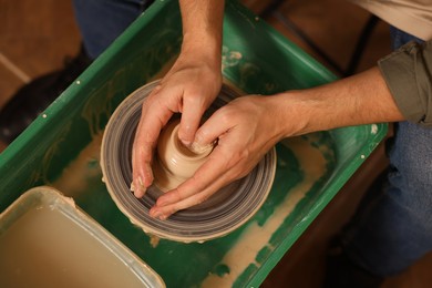 Photo of Man crafting with clay on potter's wheel, above view