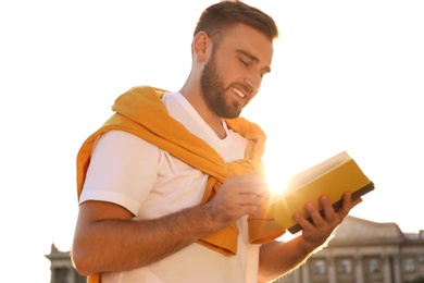 Young man reading book outdoors on sunny day