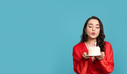 Coming of age party - 21st birthday. Woman blowing number shaped candles on cake against light blue background, space for text