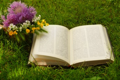 Photo of Open book and beautiful wildflowers on green grass outdoors