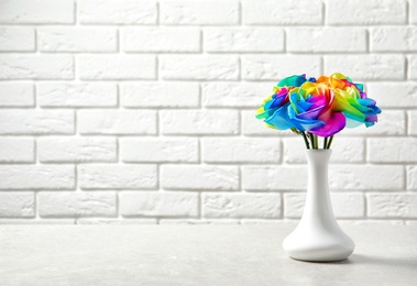 Photo of Vase with amazing rainbow rose flowers on table