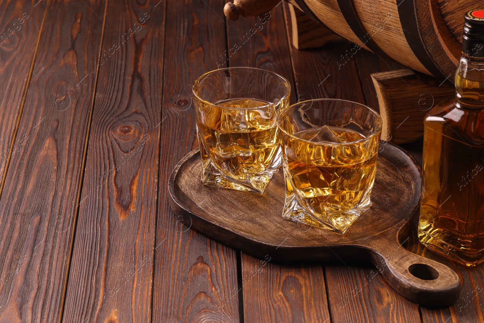 Photo of Whiskey with ice cubes in glasses and bottle on wooden table, space for text