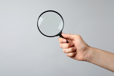 Woman holding magnifying glass on grey background, closeup. Find keywords concept