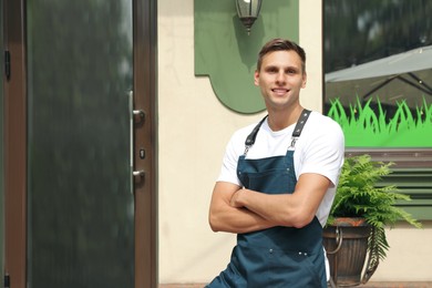 Happy young waiter in uniform near cafe, space for text
