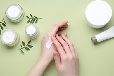 Woman applying hand cream on green background, top view