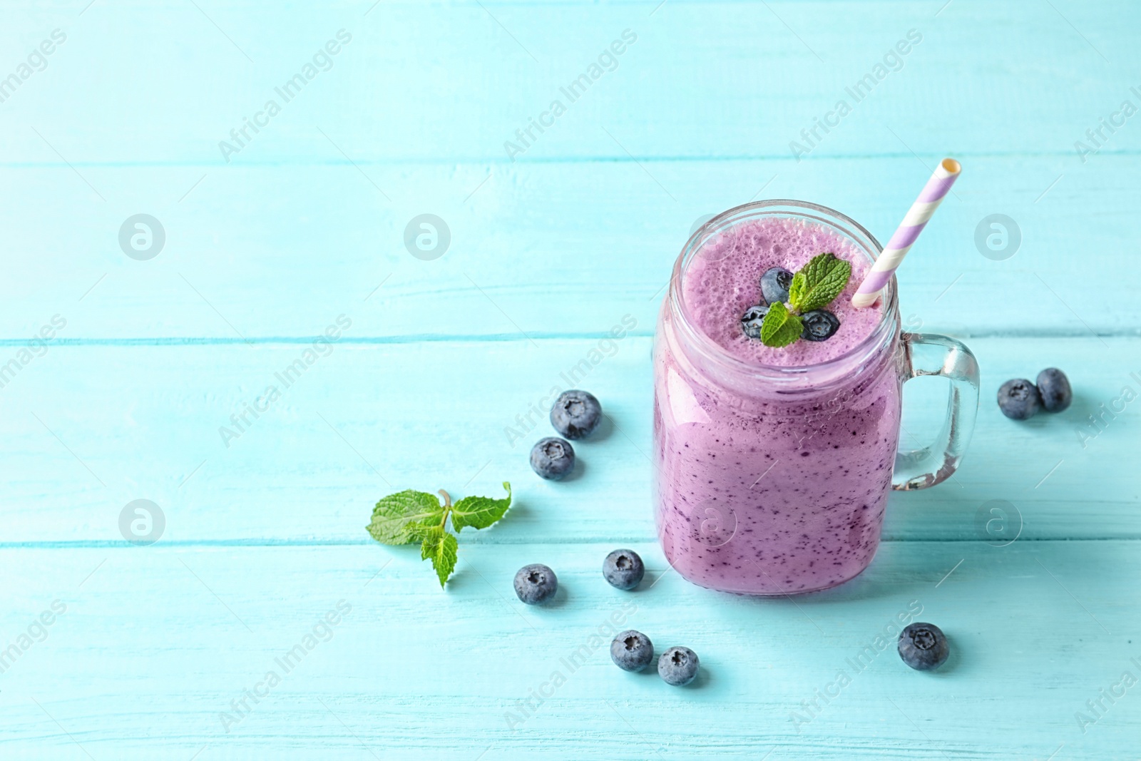 Photo of Tasty blueberry smoothie in mason jar, berries and space for text on wooden table