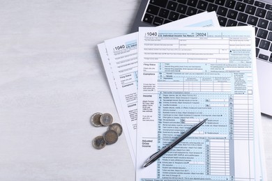 Tax forms, coins, pen and laptop on light grey table, top view. Space for text