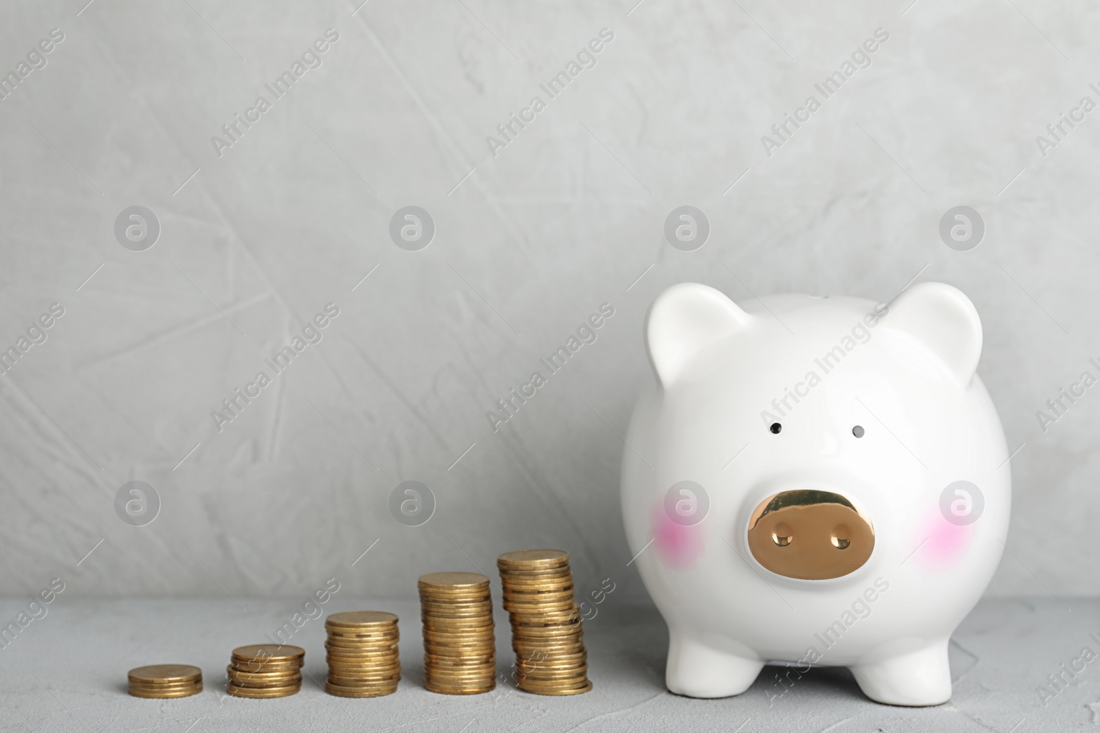 Photo of Piggy bank with coins on light table. Space for text