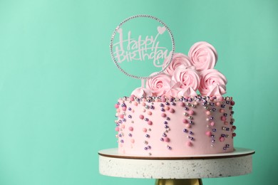 Photo of Beautifully decorated birthday cake on stand against turquoise background, space for text