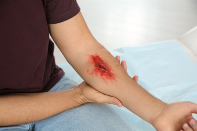 Photo of Young man with injured arm in clinic, closeup. First aid