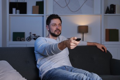 Photo of Man changing TV channels with remote control on sofa at home